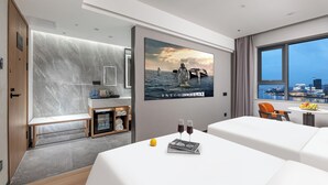 Habitación de hotel moderna con una cama grande, un escritorio pequeño, un área de descanso y vistas a la ciudad.