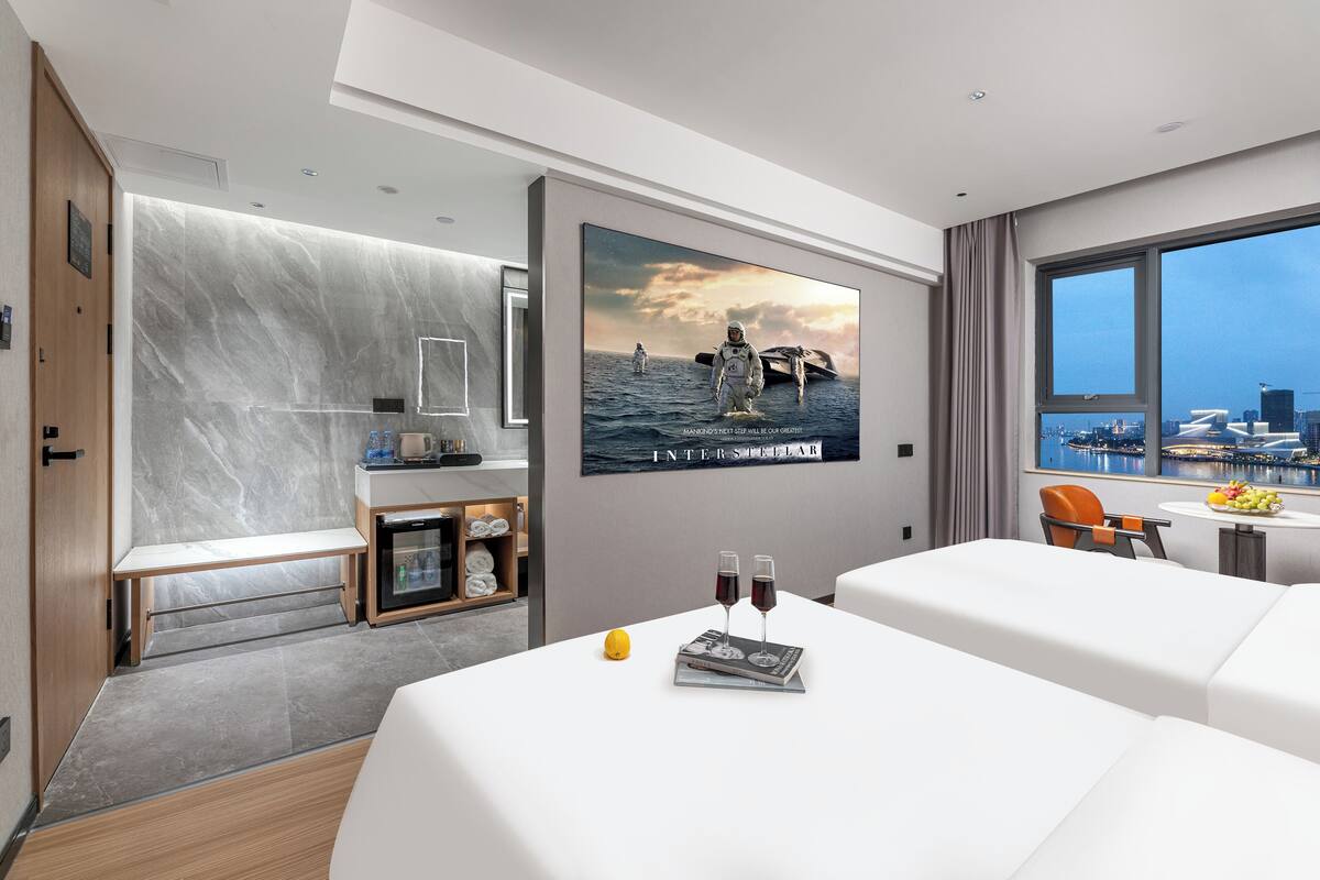 A modern hotel room with a large bed, a small desk, a seating area, and a city view.