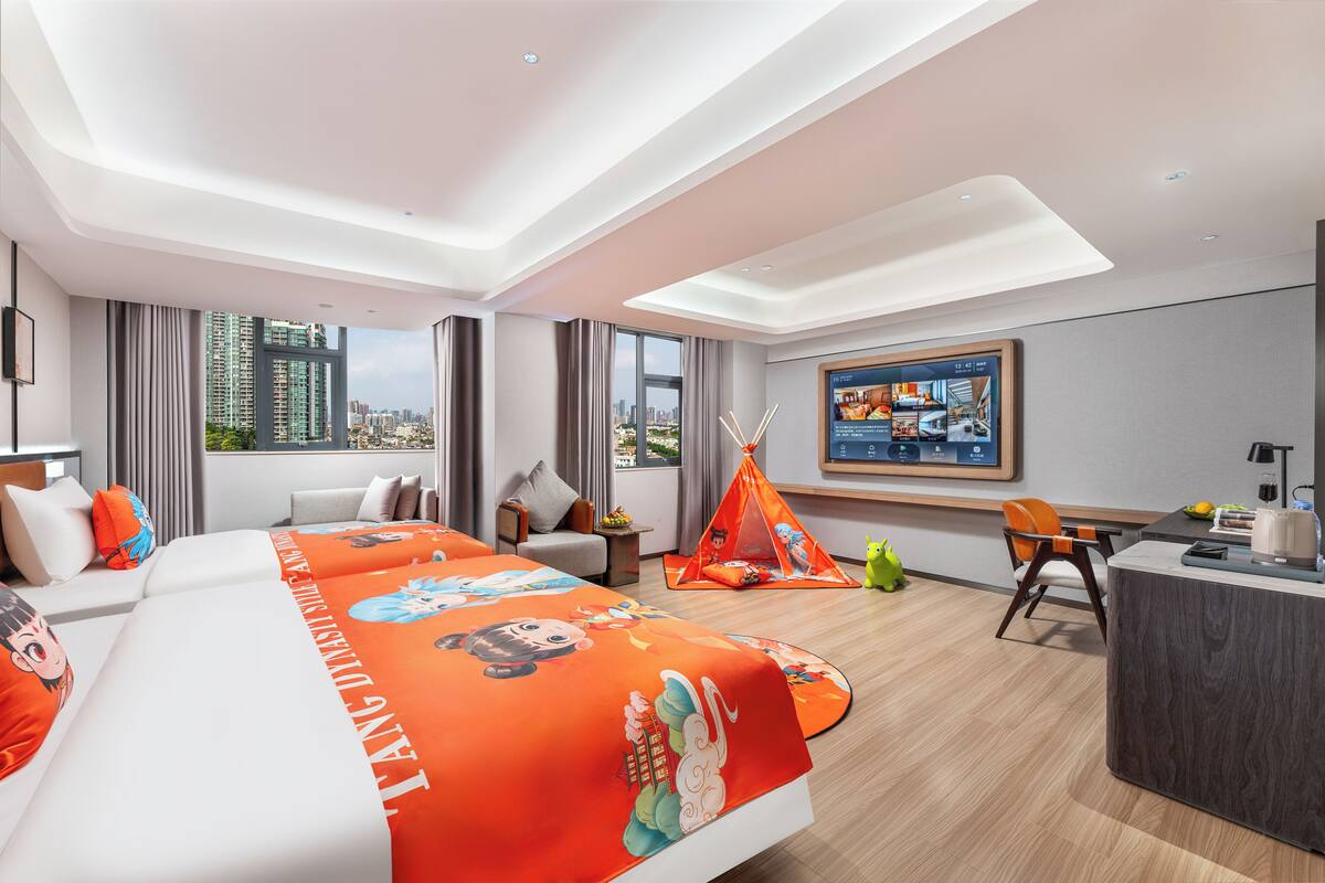 A hotel room with a large bed, a desk, a chair, a small table, a window with a city view, and a painting on the wall.
