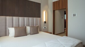 Une chambre d’hôtel moderne avec un grand lit, une tête de lit à lattes verticales, une table de chevet et une petite table d’appoint.