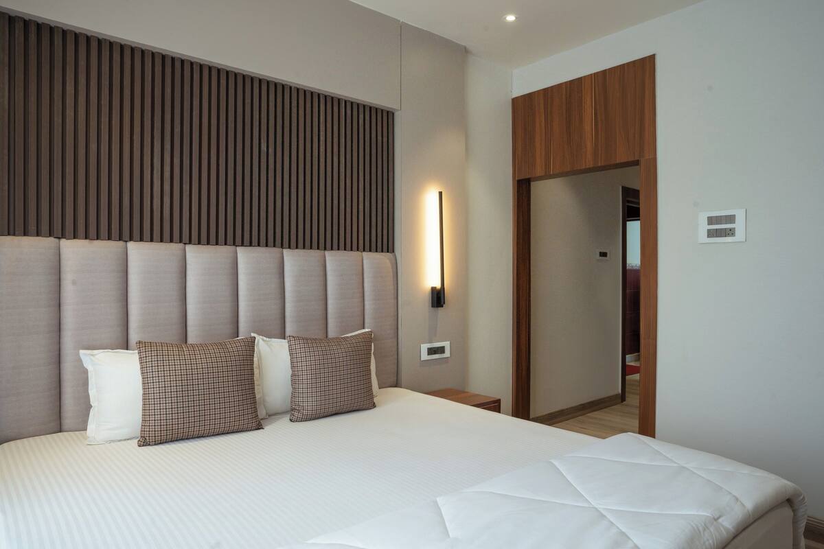 Une chambre d’hôtel moderne avec un grand lit, une tête de lit à lattes verticales, une table de chevet et une petite table d’appoint.