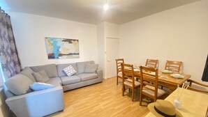 Een woonkamer met een grijze bank, een eettafel met houten stoelen en een houten vloer.