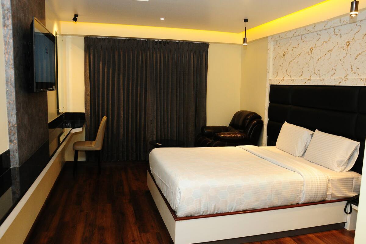 A hotel room with a bed, a chair, a desk, a TV, and a curtain.