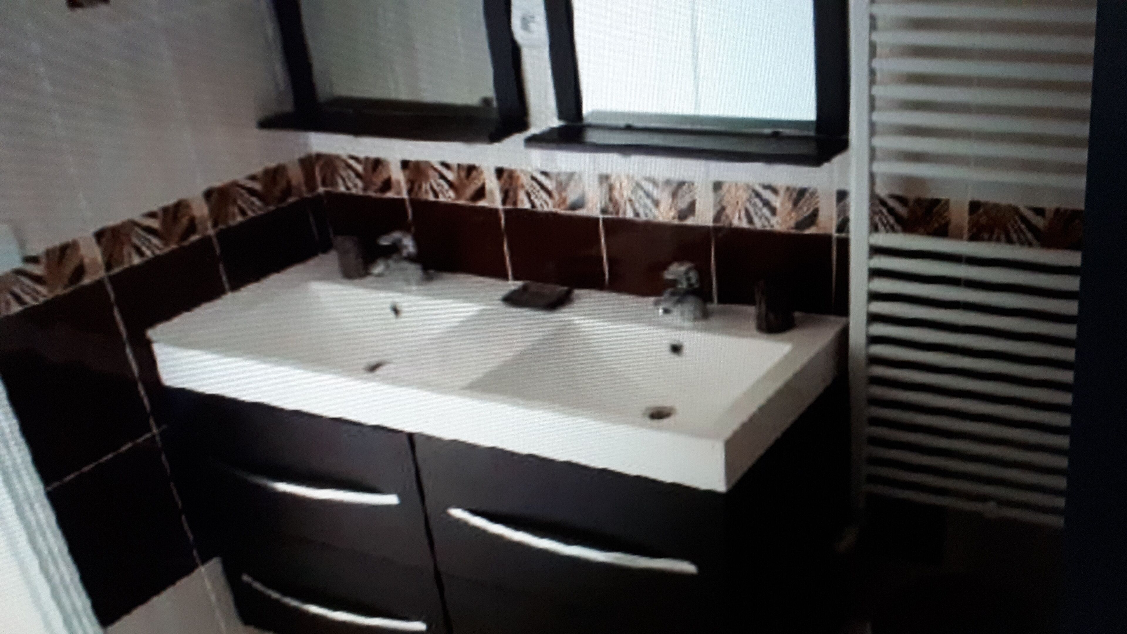 Une salle de bain avec un double lavabo, des meubles sombres et des carreaux à motifs.