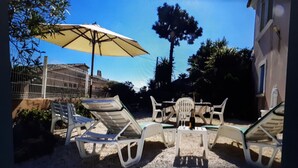 Eine Terrasse mit Tisch und Stühlen, einem großen Sonnenschirm und einem eingezäunten Bereich mit einem Baum.