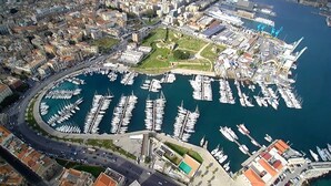 Vista aérea de un puerto deportivo con numerosas embarcaciones amarradas, rodeado de edificios urbanos y una carretera.