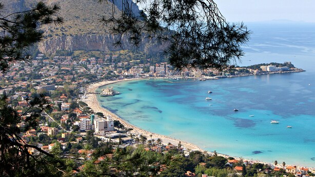 Un pueblo costero con playa, aguas azul turquesa y montañas al fondo.
