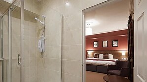A hotel room with a shower, a bed with a headboard, a bedside table, and a chair.