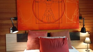 A bed with two red pillows, a wooden headboard, and a large orange artwork depicting a human figure. - House in El Bosque Encantado (San Martín de Valdeiglesias)
