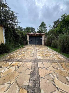 Ein gepflasterter Weg führt zu einer Garage mit einem Ziegeldach, umgeben von viel Grün.