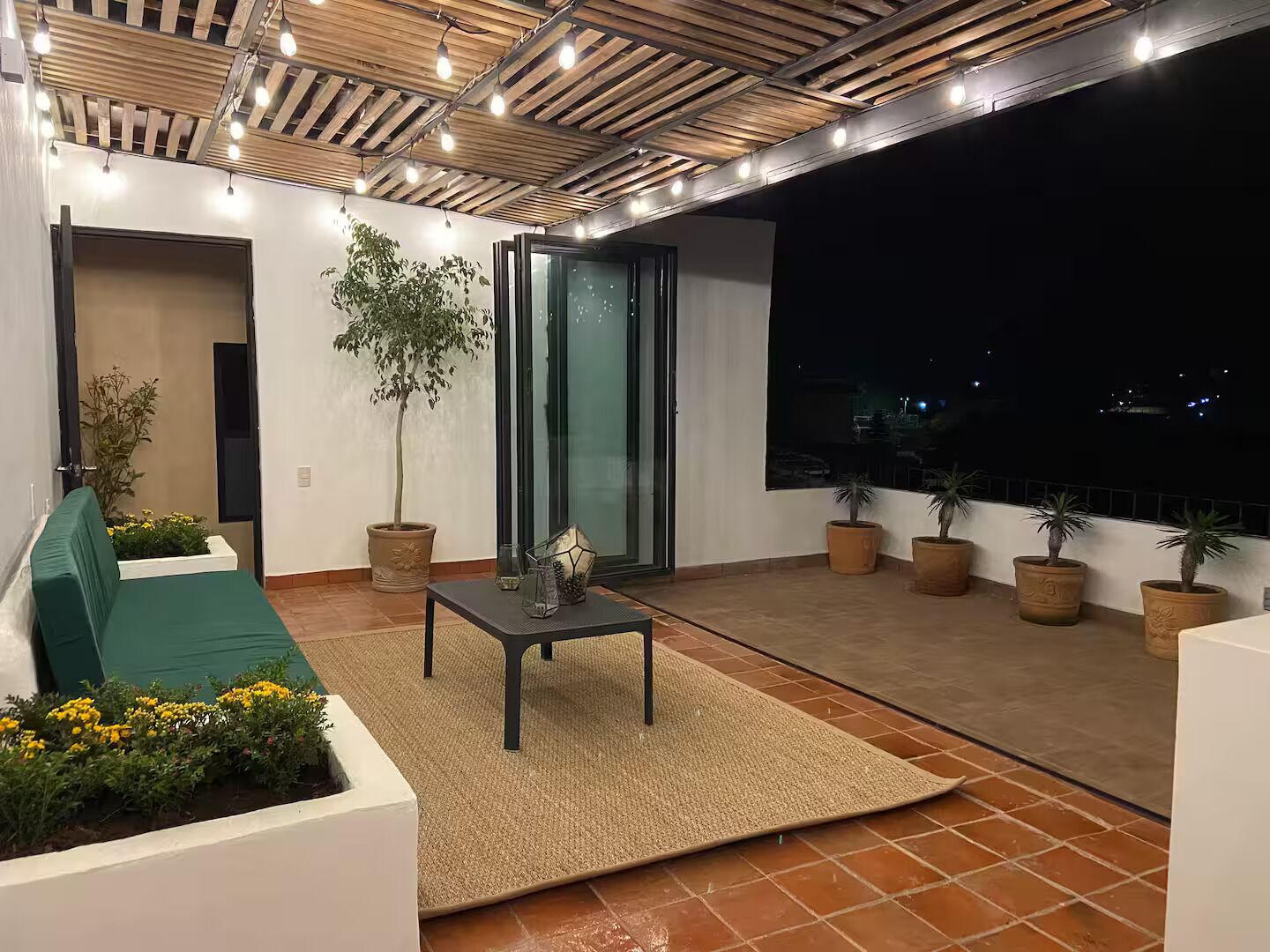 Un balcon avec un canapé, une table, des plantes en pot et une vue sur la ville la nuit.