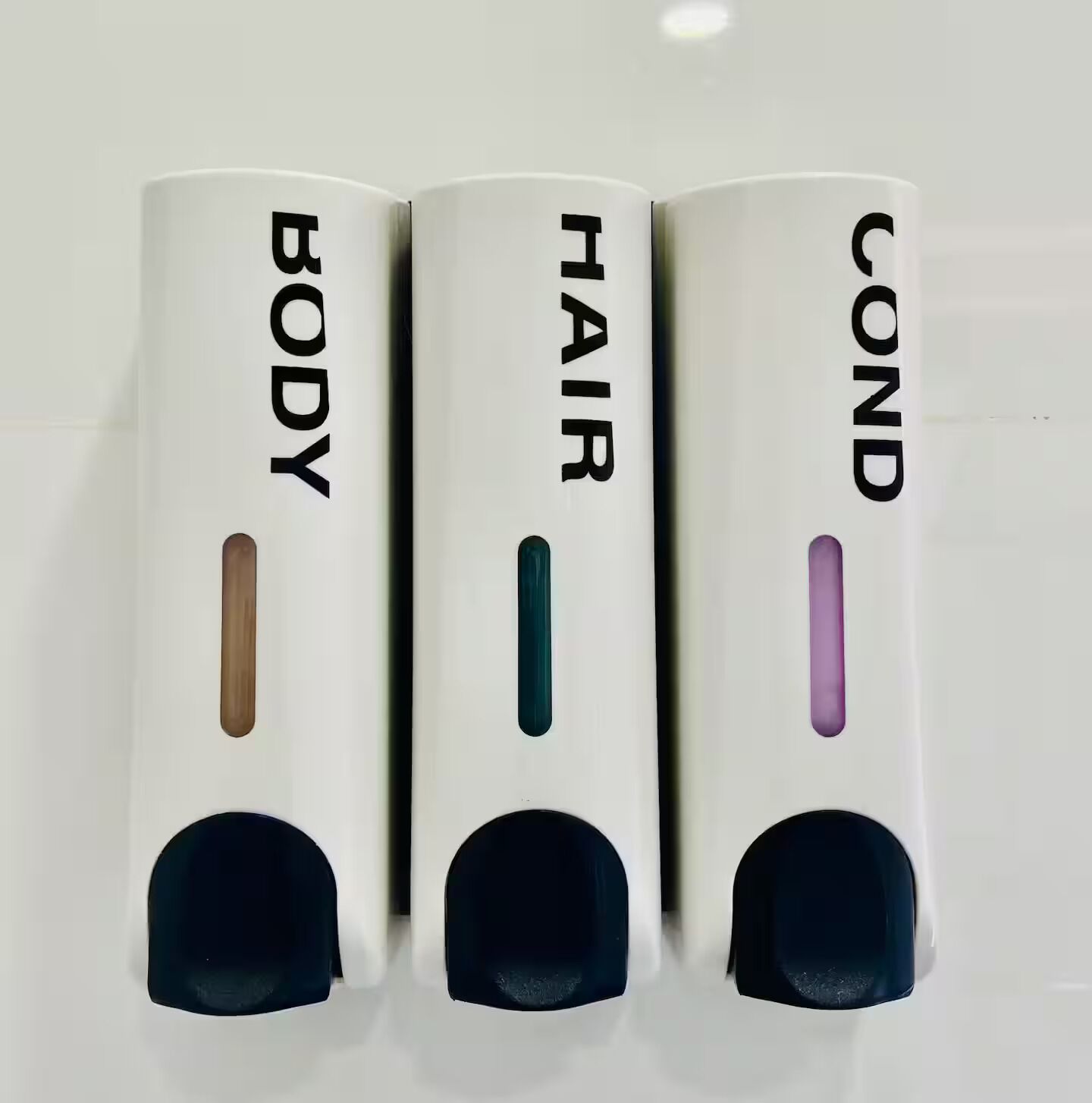 Three white dispensers with labels 'BODY,' 'HAIR,' and 'COND' on a white surface.
