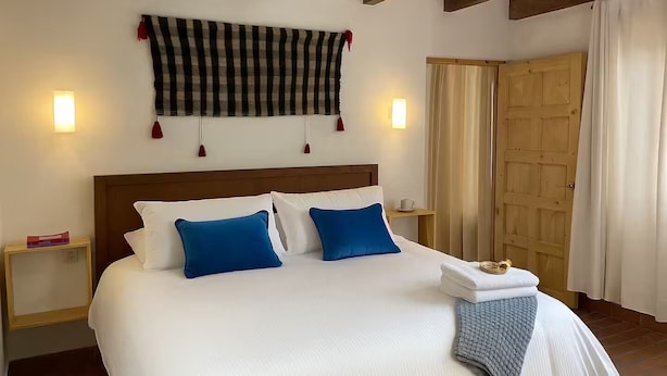 Ett hotellrum med en stor säng, två sängbord, en träpanel vid sänggaveln, en rutig gardin och en trädörr.