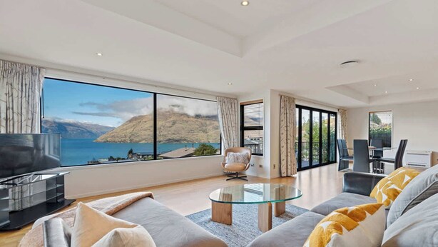 A modern living room with a large window offering a scenic view of a lake and mountains. - Elevated Elegance in Fernhill (Queenstown)