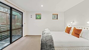A bedroom with a large bed, two windows, and a sliding glass door leading to an outdoor area. - Elevated Elegance in Fernhill (Queenstown)
