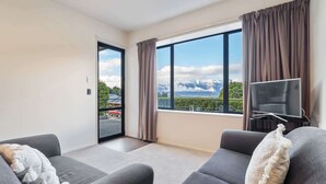 Un salon moderne avec deux canapés gris, un téléviseur à écran plat et une grande fenêtre donnant sur un paysage montagneux.