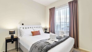 Une chambre d’hôtel avec un lit, deux tables de chevet, une fenêtre avec des rideaux et une vue sur la ville.