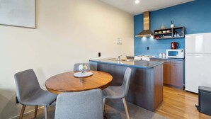Une cuisine compacte dotée d’un îlot central, de chaises grises, d’une table à manger en bois et d’un mur d’accent bleu.
