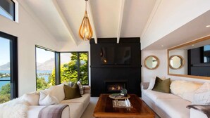 A modern living room with two sofas, a wooden coffee table, a fireplace, and large windows offering a scenic view.