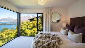 A bedroom with a large window, a chandelier, a round mirror, and a bed with a fur throw.