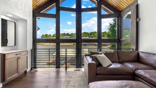 A spacious room with a large window, a brown leather sofa, and a wooden ceiling. - Cozy in a Cove – 14 ppl Stay (Camdenton)