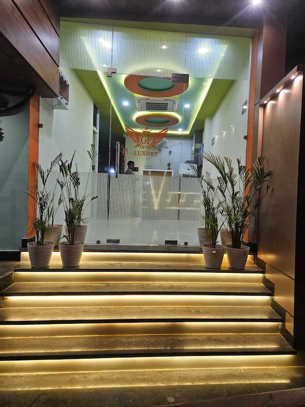 Zona de recepción de hotel con diseño moderno, que incluye un mostrador de recepción, una escalera con escalones iluminados y plantas en macetas.