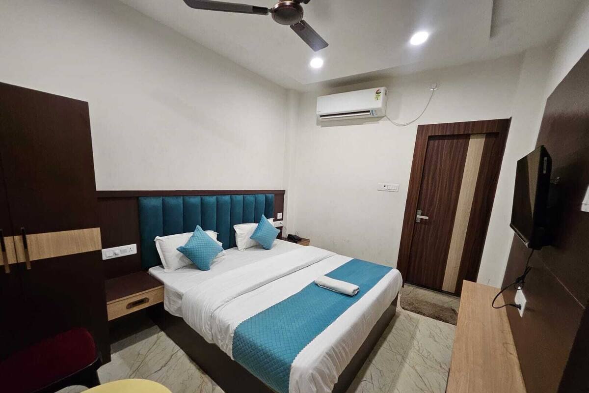 A hotel room with a bed, a desk, a chair, a TV, an air conditioner, and a ceiling fan.