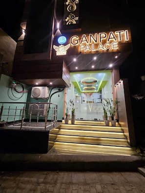 Entrada del Palacio Ganpati con señalización iluminada, una escalera y plantas en macetas.