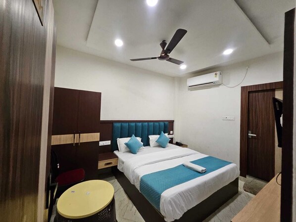 A hotel room with a bed, a ceiling fan, an air conditioning unit, a small round table, and a TV.