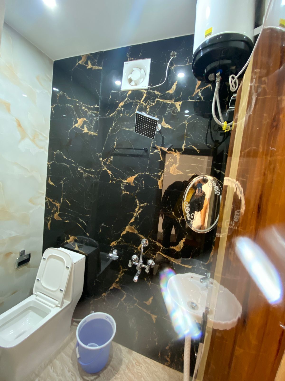 A bathroom with a black marble wall, a white toilet, a bidet, a shower, and a mirror.