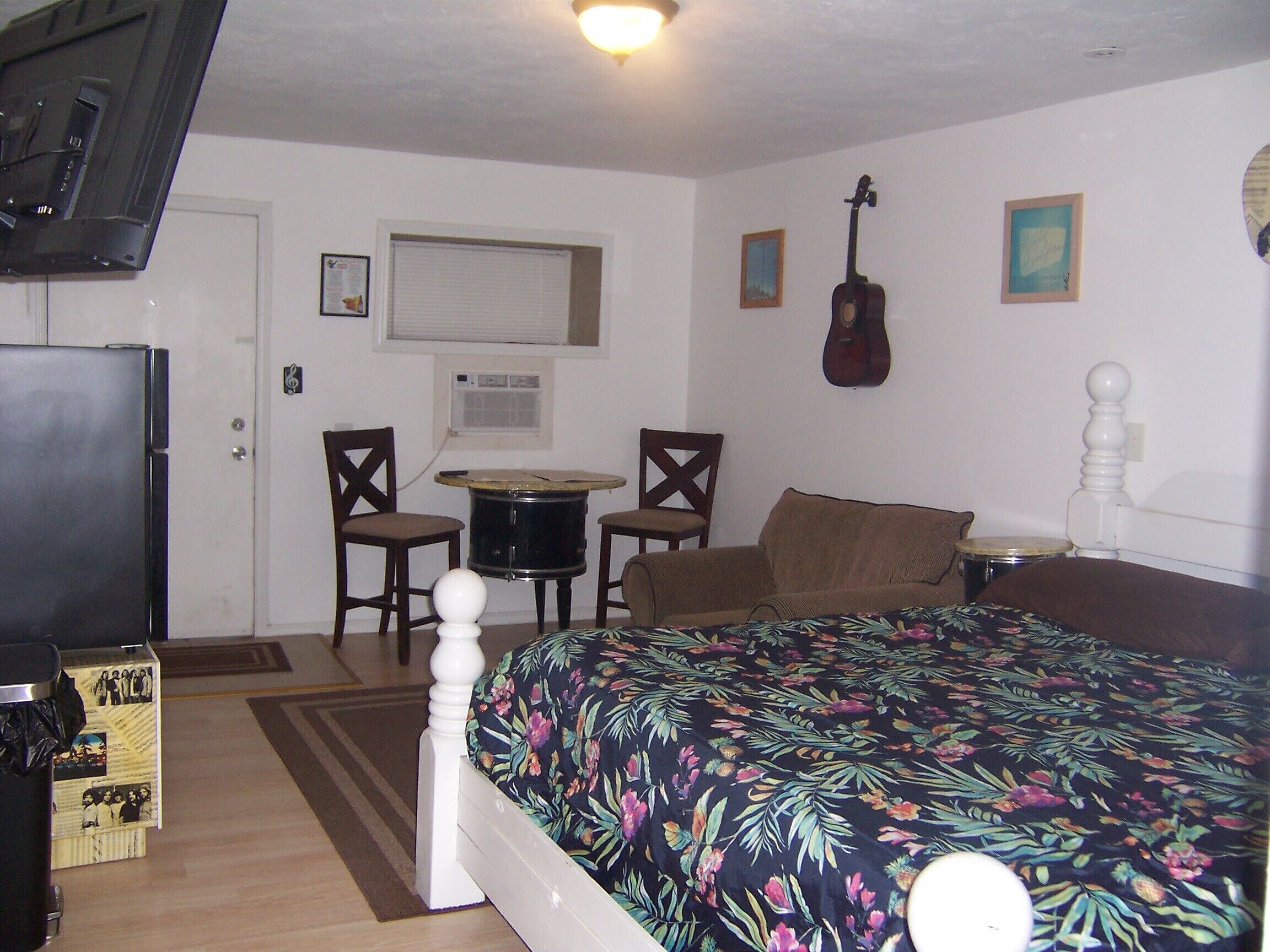 A bedroom with a bed, a drum set, and a guitar.