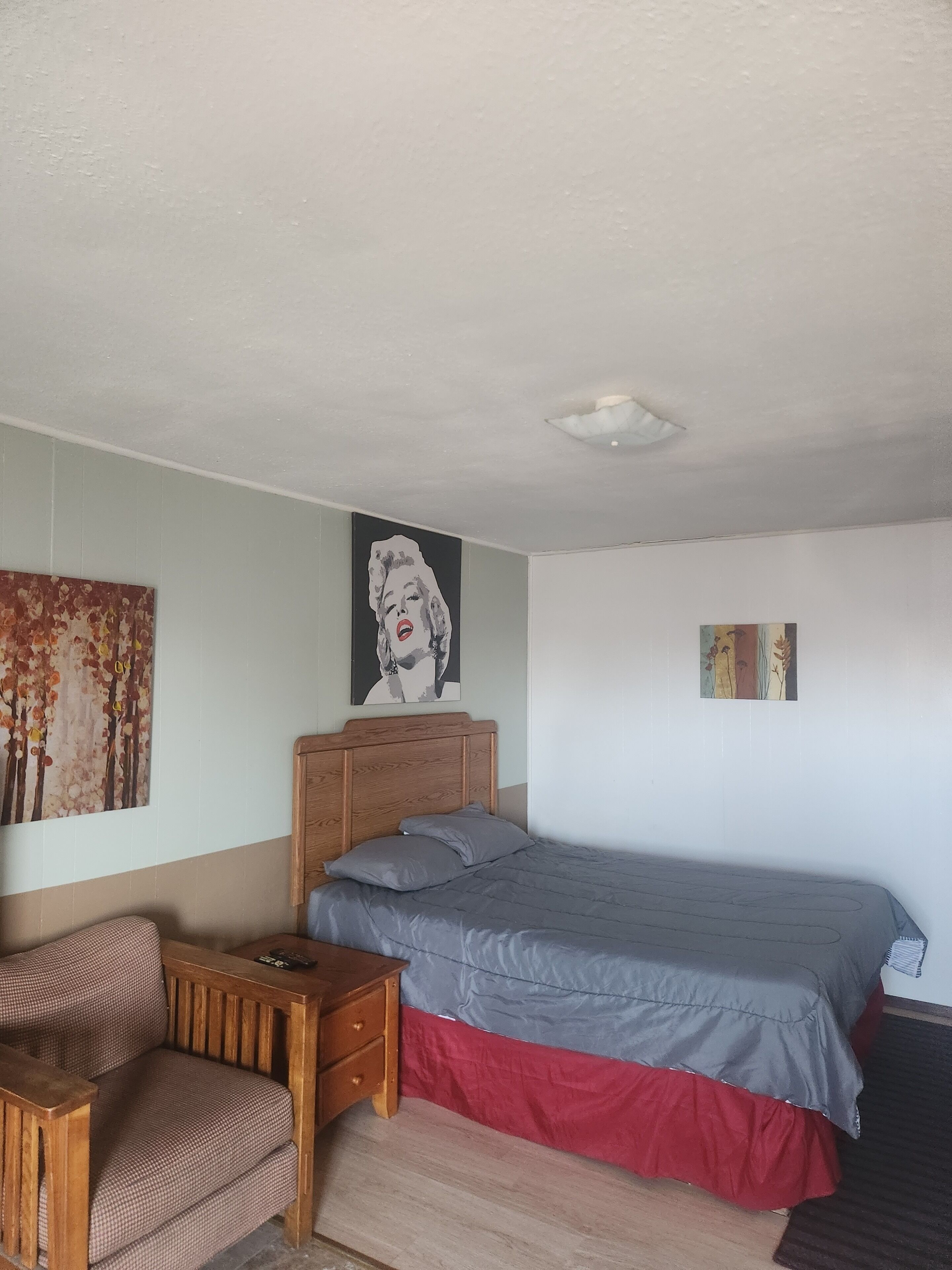 A bedroom with a bed, a wooden nightstand, a chair, and two wall art pieces.