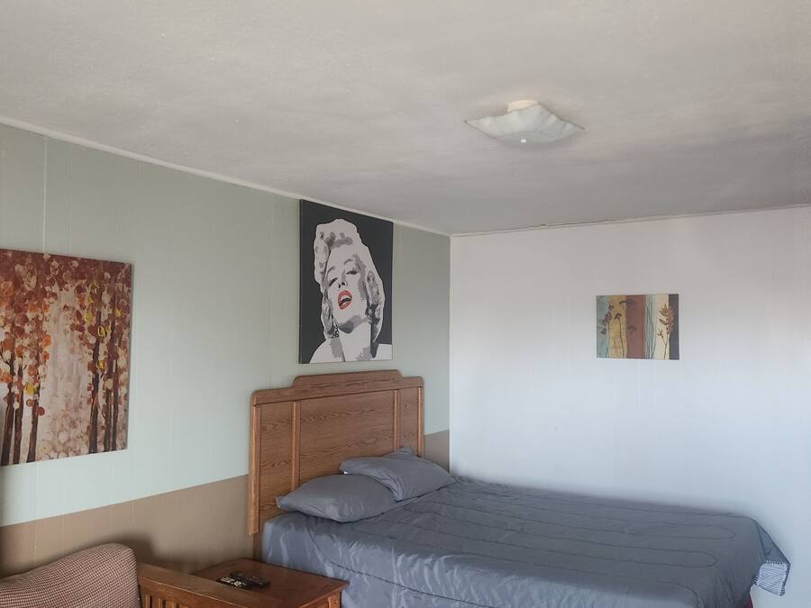 A bedroom with a bed, a wooden nightstand, a chair, and two wall art pieces.