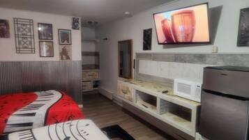 A compact room with a bed, a flat-screen TV mounted on the wall, a microwave, and a refrigerator.