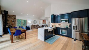 Una cocina moderna con armarios oscuros, electrodomésticos de acero inoxidable y una mesa de comedor de madera con sillas azules.