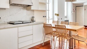 Une cuisine moderne avec des armoires blanches, une cuisinière encastrée et un coin repas comprenant des chaises en osier et une table en bois.