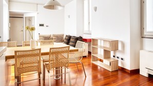 Un salon moderne avec une table à manger en bois, des chaises en osier, un canapé agrémenté d’un coussin à carreaux et une bibliothèque intégrée en bois.