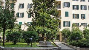 Une cour intérieure avec une fontaine centrale, entourée de verdure et bordée d’un bâtiment doté de nombreux balcons.
