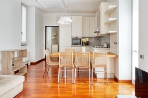 A modern kitchen with a dining area, wooden flooring, and a large window. - JOIVY Bright Flat near Parco Sempione (Milan)