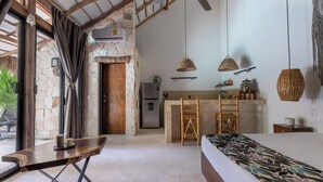 Un dormitorio con cama, escritorio y una kitchenette al fondo.