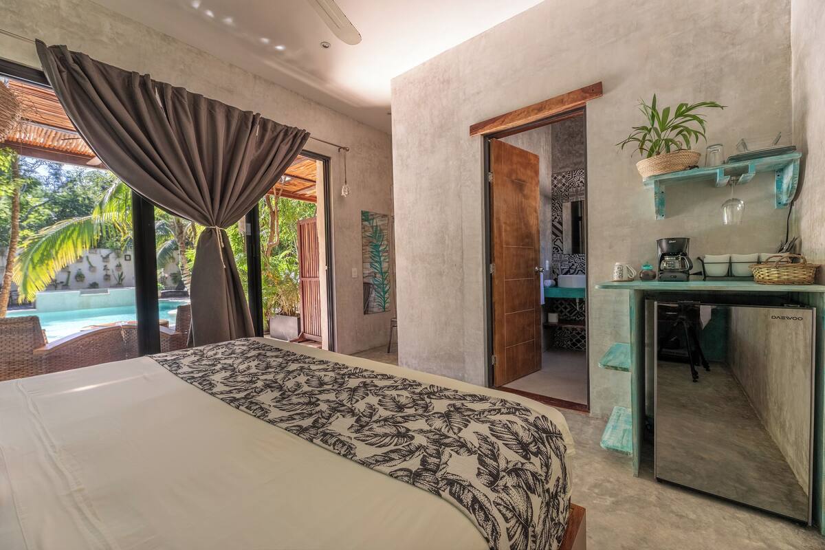 A bedroom with a bed, a desk with a mirror, and a view of an outdoor swimming pool.