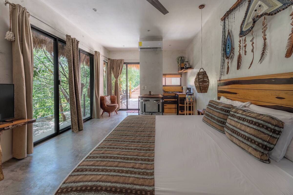 A modern hotel room with a large bed, a TV, and a view of the outdoors.
