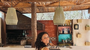 Una persona sentada en un bar con una pared de azulejos coloridos, techo de madera rústica y lámparas colgantes.