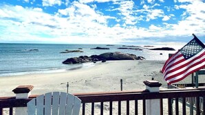 A beach view with an American flag, a wooden deck, and a white chair. - Ocean front Scituate Minot Beach Front Sleeps 11 (Scituate)
