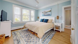 Un dormitorio con cama, televisión, ventana, ventilador de techo y puerta.
