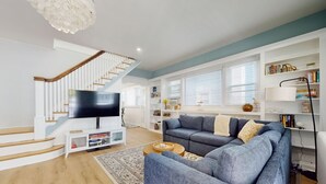 Una sala de estar moderna con una escalera, un televisor de pantalla plana, un sofá gris y una estantería.