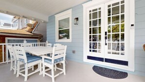 Un patio techado con una mesa y sillas blancas, una puerta grande de color blanco y una ventana pequeña.