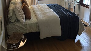 Ein Schlafzimmer mit einem Bett, einem Nachttisch, einem Schreibtisch, einem Deckenventilator und einem Fenster mit Vorhängen.