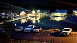 A parking lot with several cars, a building with a sign that reads "Waterside Marina," and a body of water reflecting the lights.