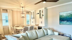 A living room with a white sectional sofa, a dining area with a white table and chairs, and a ceiling fan.